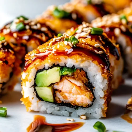Close-up of a salmon tempura sushi roll with cucumber, drizzled with eel sauce and topped with sesame seeds and green onions.