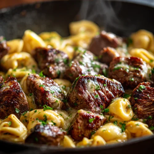 Garlic butter steak bites with cheese tortellini in a cast iron skillet.