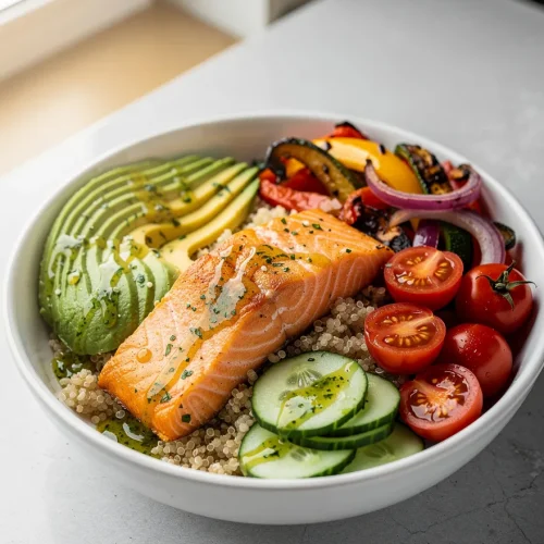 Salmon quinoa bowl with avocado, cucumbers, roasted vegetables, cherry tomatoes, and quinoa.