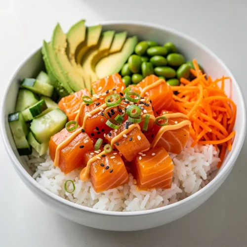 Spicy salmon bowl recipe with sushi rice, avocado, cucumber, edamame, carrots, and sesame-topped salmon.